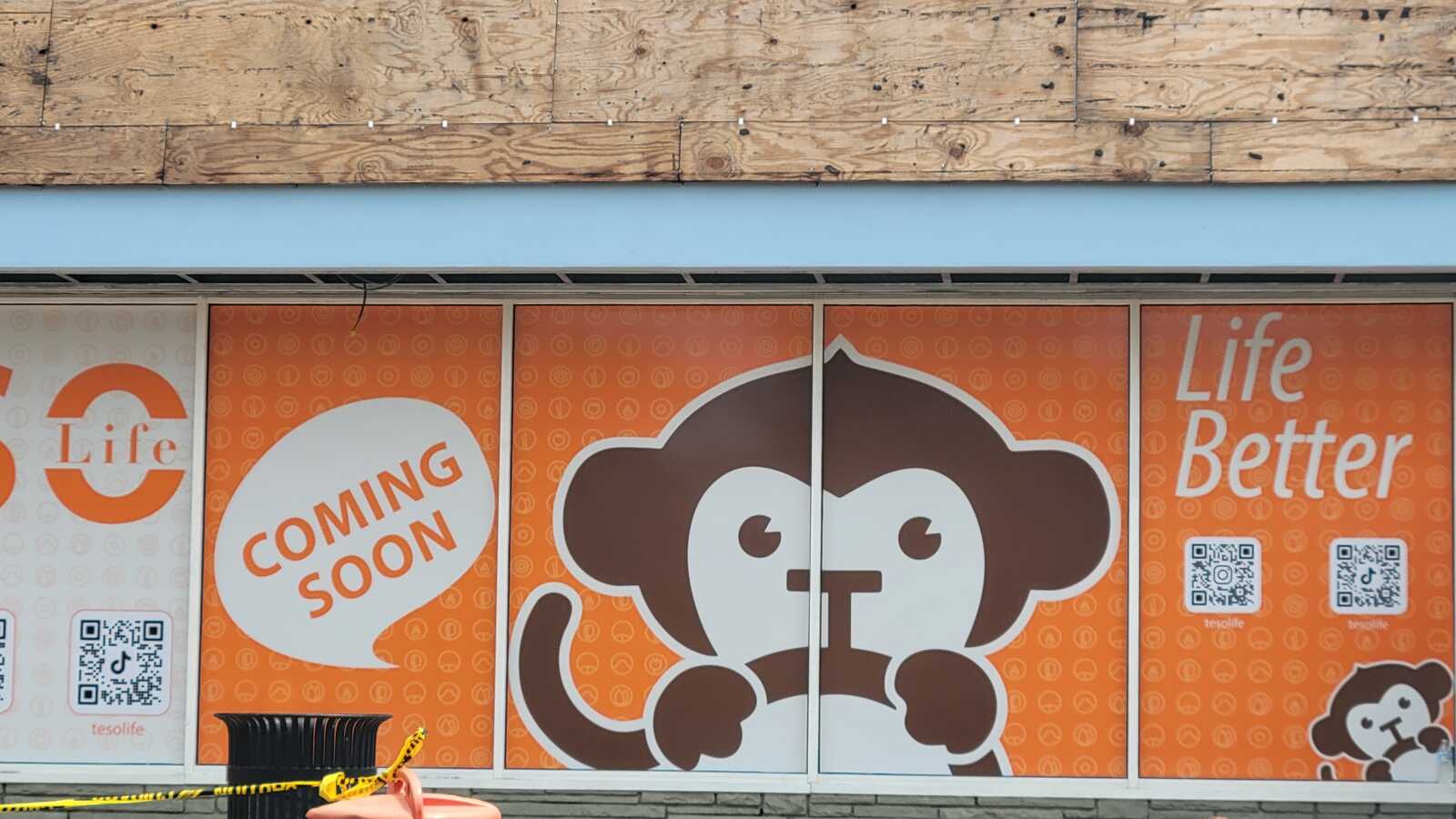 An orange and white "coming soon" sign with a cartoon monkey, two bar codes, and the words "Life Better"