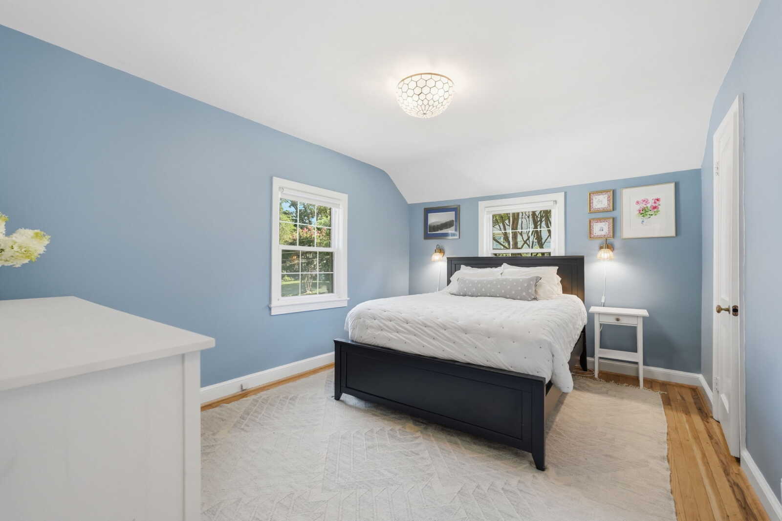 Blue-painted bedroom with a dark wood bed and white bedding, flanked by white nightstands and framed art above.