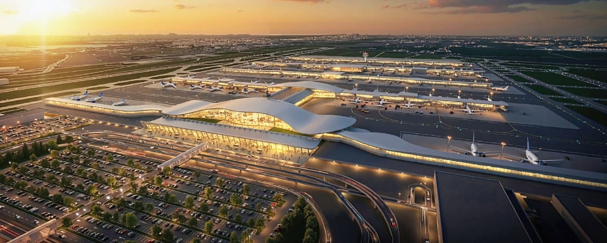 A large modern airport with curved, illuminated terminals at sunset and planes parked at gates.