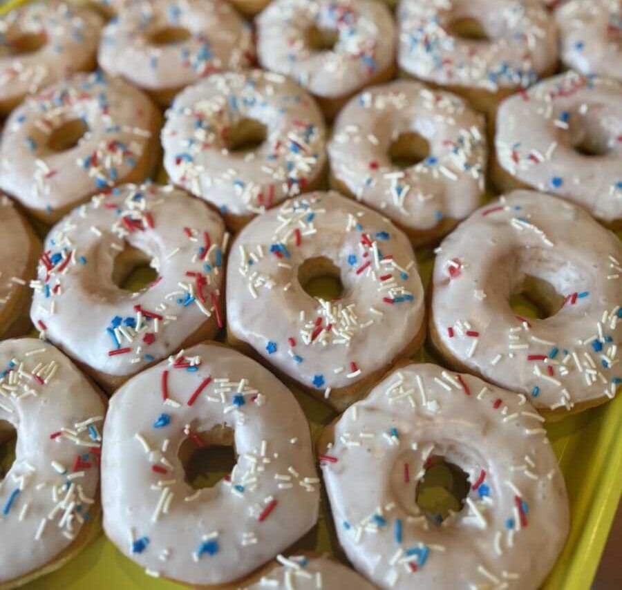 White frosted donuts with red, white, and blue sprinkles on a yellow tray