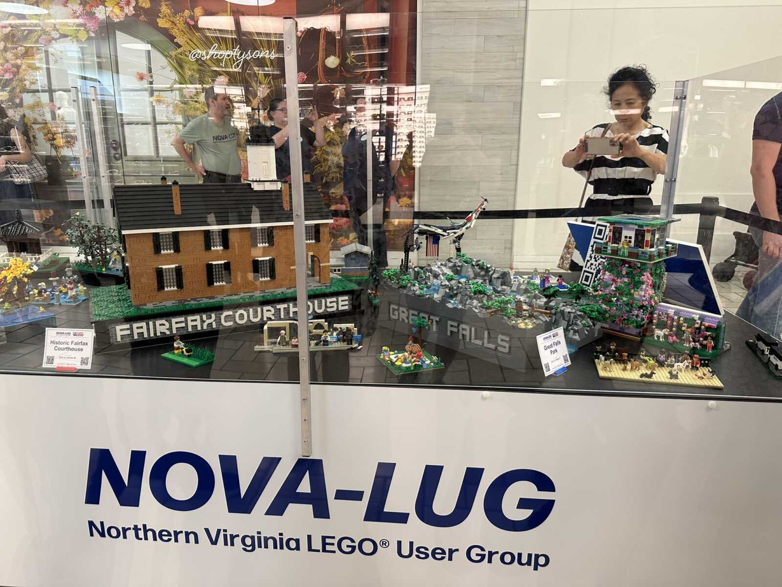 LEGO diorama featuring a brick courthouse with 'Fairfax Courthouse' label, greenery and small figures on a display case at a NOVA-LUG event.