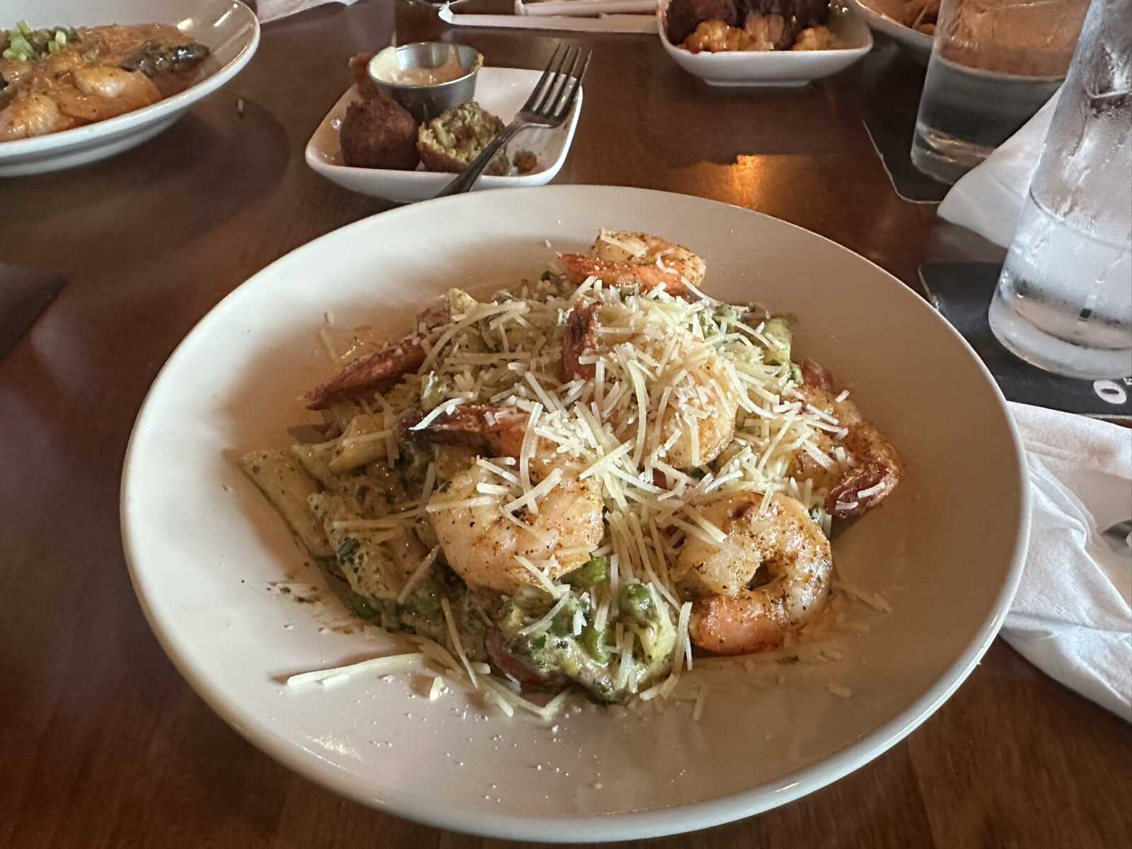 Shrimp pasta with grated cheese and broccoli in a white bowl on a wooden table