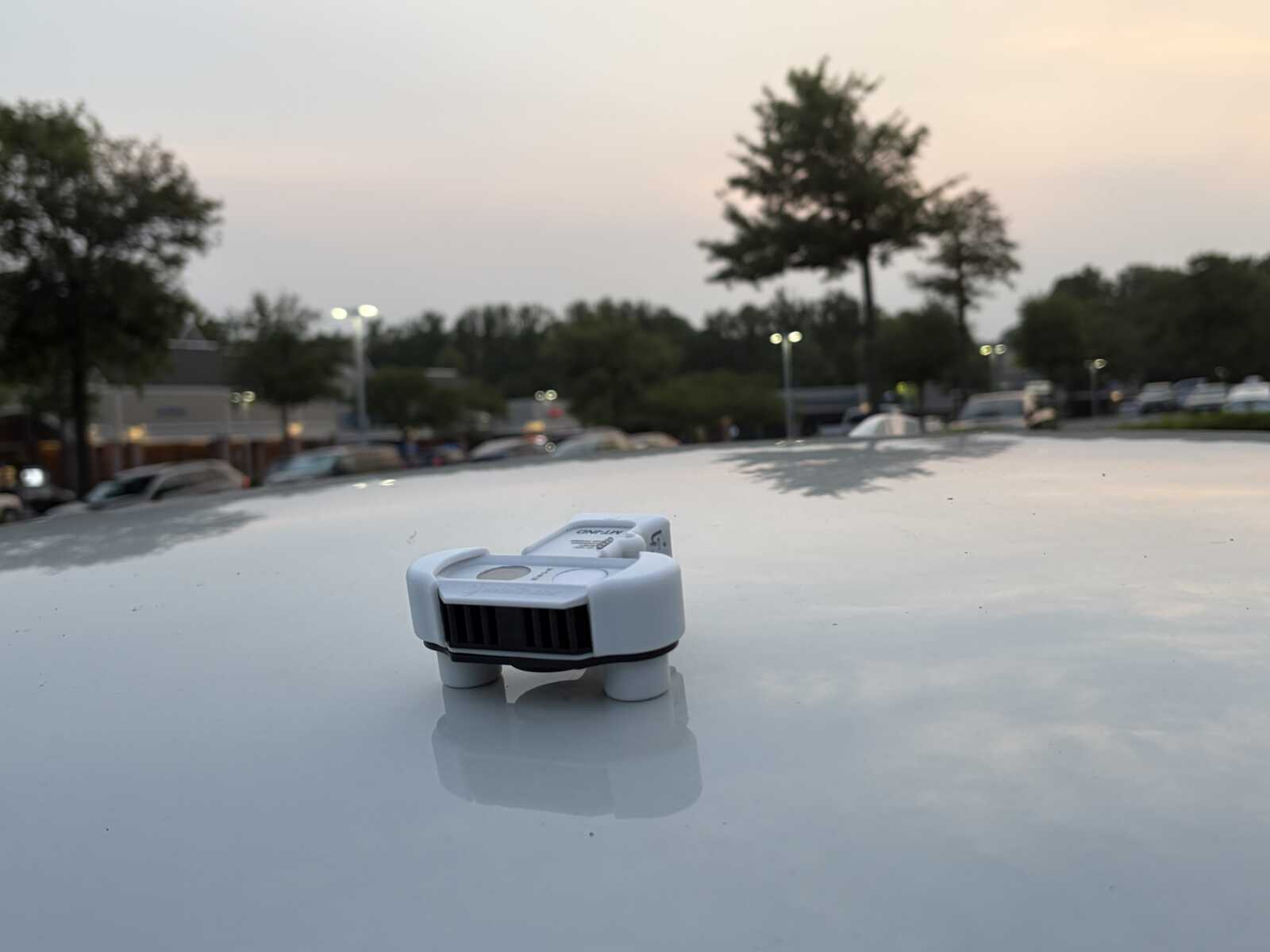Vehicle rooftop heat data sensor (courtesy Faith Alliance for Climate Solutions) | FFXnow Small white sensor device mounted on a car hood in a parking lot at sunset, with trees in the background.