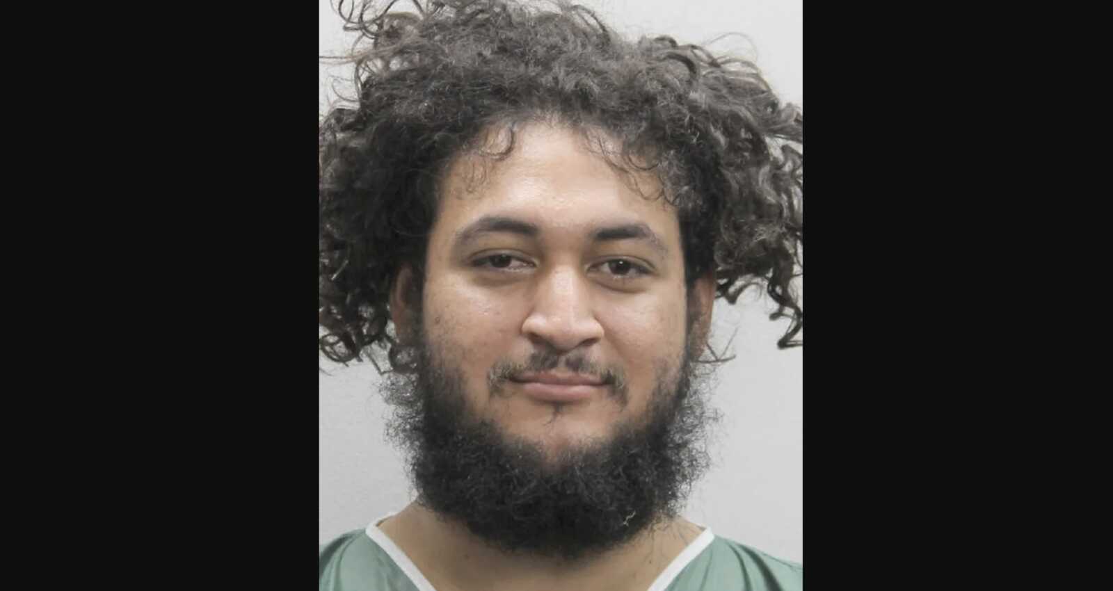 Mugshot of a man with curly hair and a full beard, wearing a green shirt, against a plain light background.