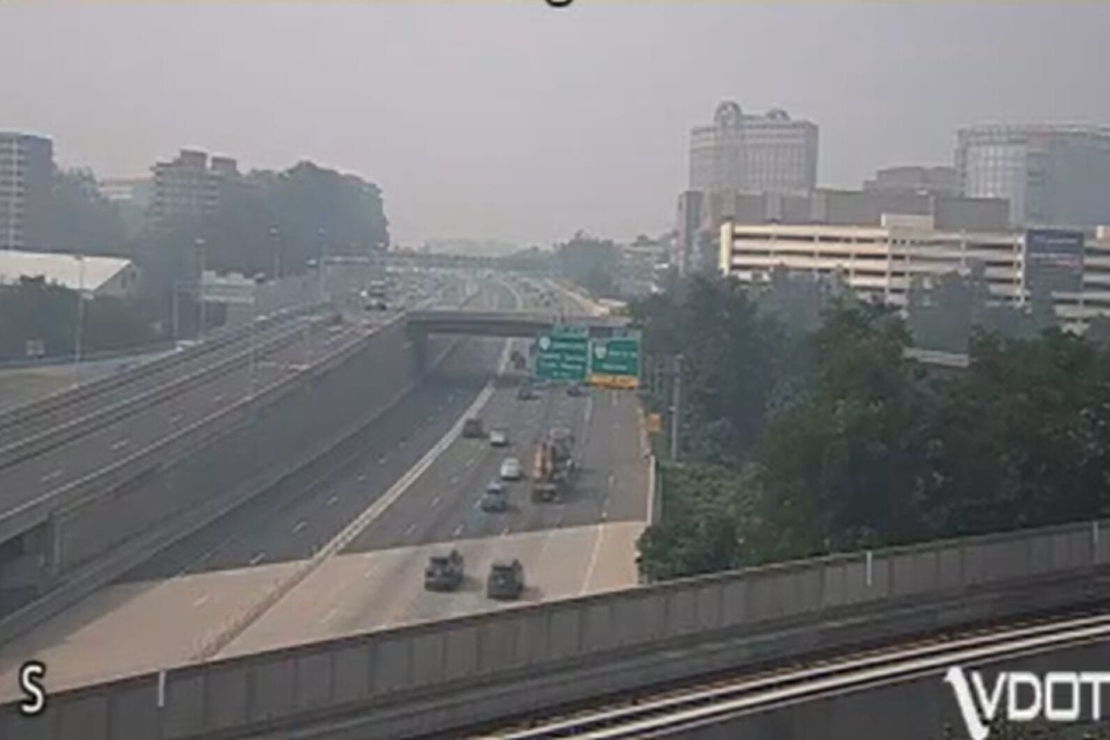 Wide view of a multi-lane urban highway with an overpass, light traffic, and a hazy city skyline in the distance.