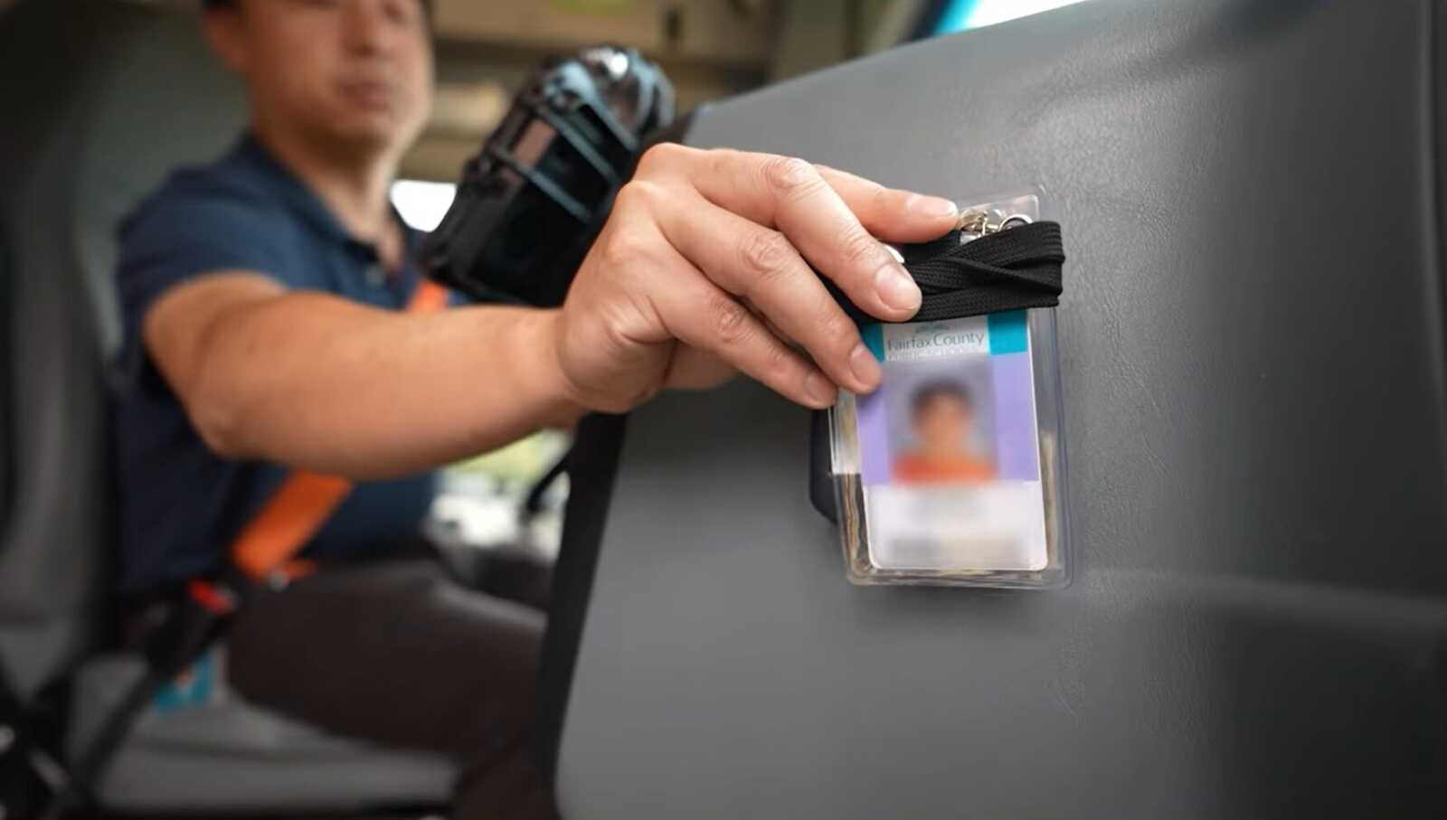 Person in uniform attaches or reveals a blurred ID badge in a clear plastic holder clipped to a gray surface, focus on hand and badge