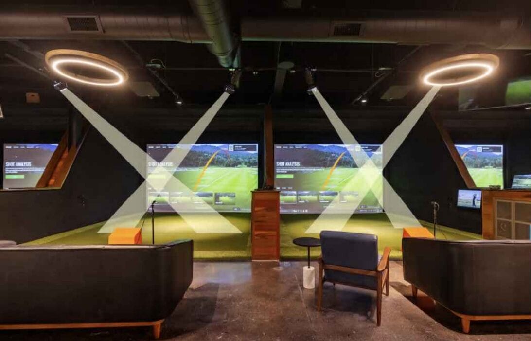 Indoor golf simulator room with multiple screens showing a virtual course and a central podium.