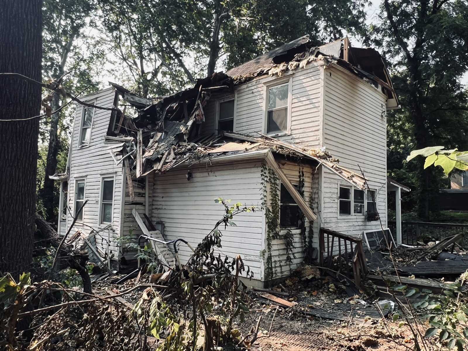 Two-story white wooden house with a collapsed roof and extensive debris surrounding the structure.