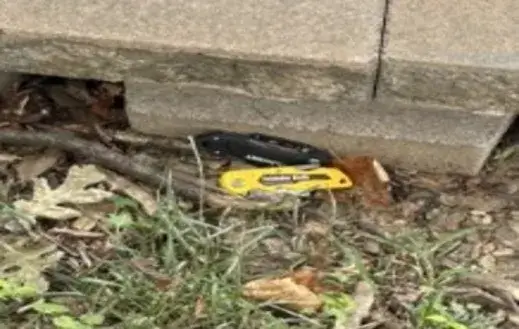 Yellow utility knife lying on dirt and grass beside a row of concrete blocks.