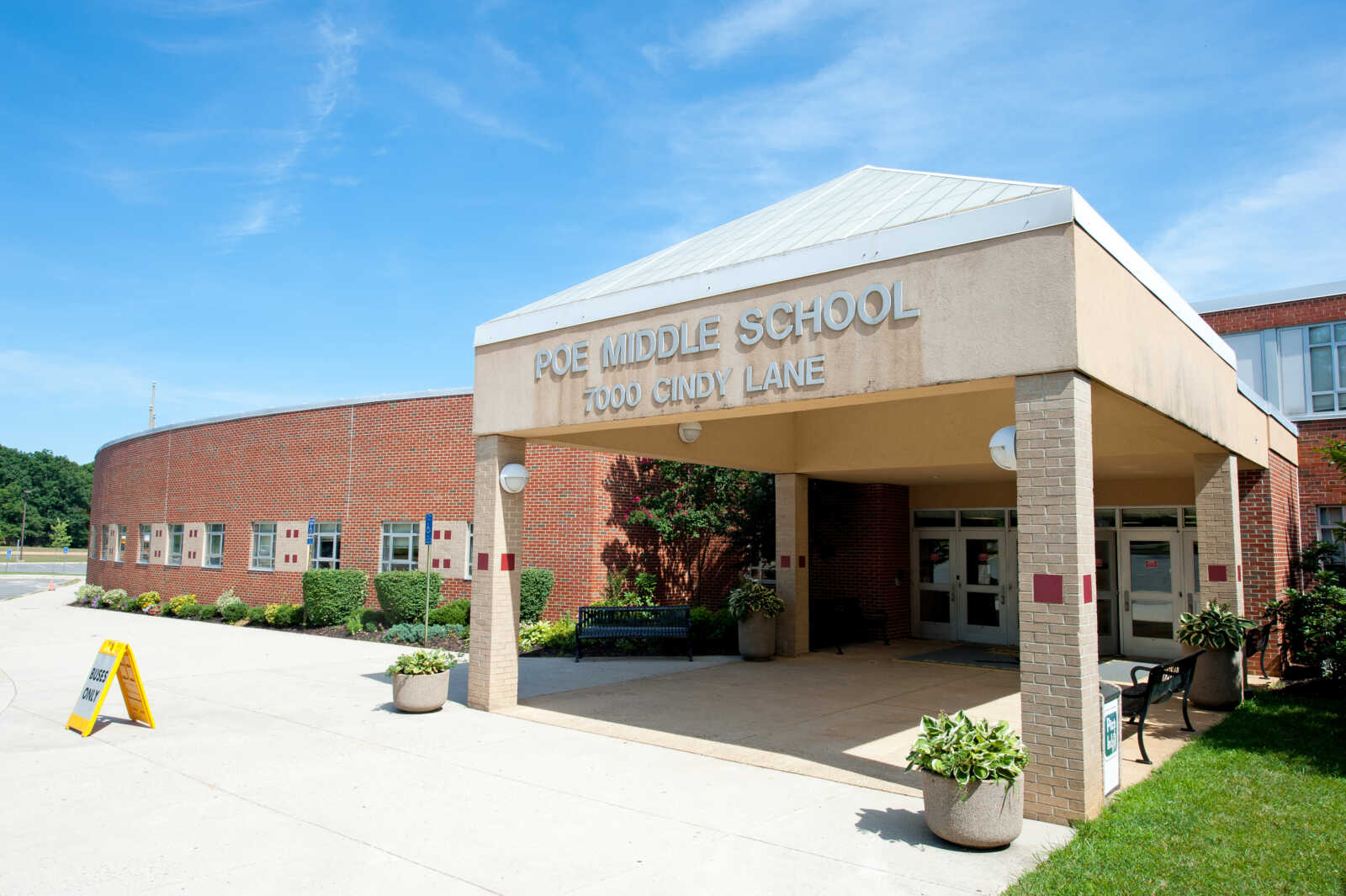 Entrance to Poe Middle School in Annandale (courtesy FCPS) | FFXnow Front entrance of Poe Middle School with a beige porte-cochère and the sign 'POE MIDDLE SCHOOL 7000 CINDY LANE' above the doors, brick wall facade, sunny day.