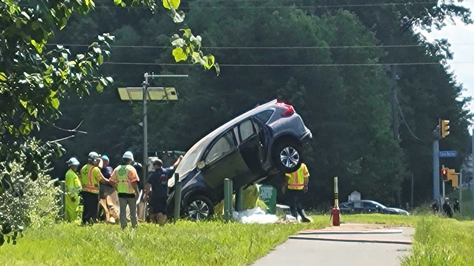 SUV perched on a street curb/green post with a group of rescue workers around it