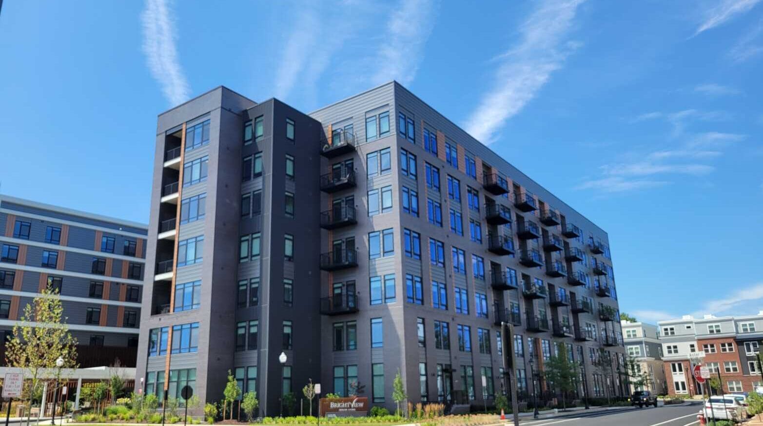 Modern multi-story apartment building with balconies under a clear blue sky, urban neighborhood in the foreground.