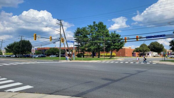 Image of a crosswalk with students visible in the distance walking across the road. A brick high school building is visible in the background.