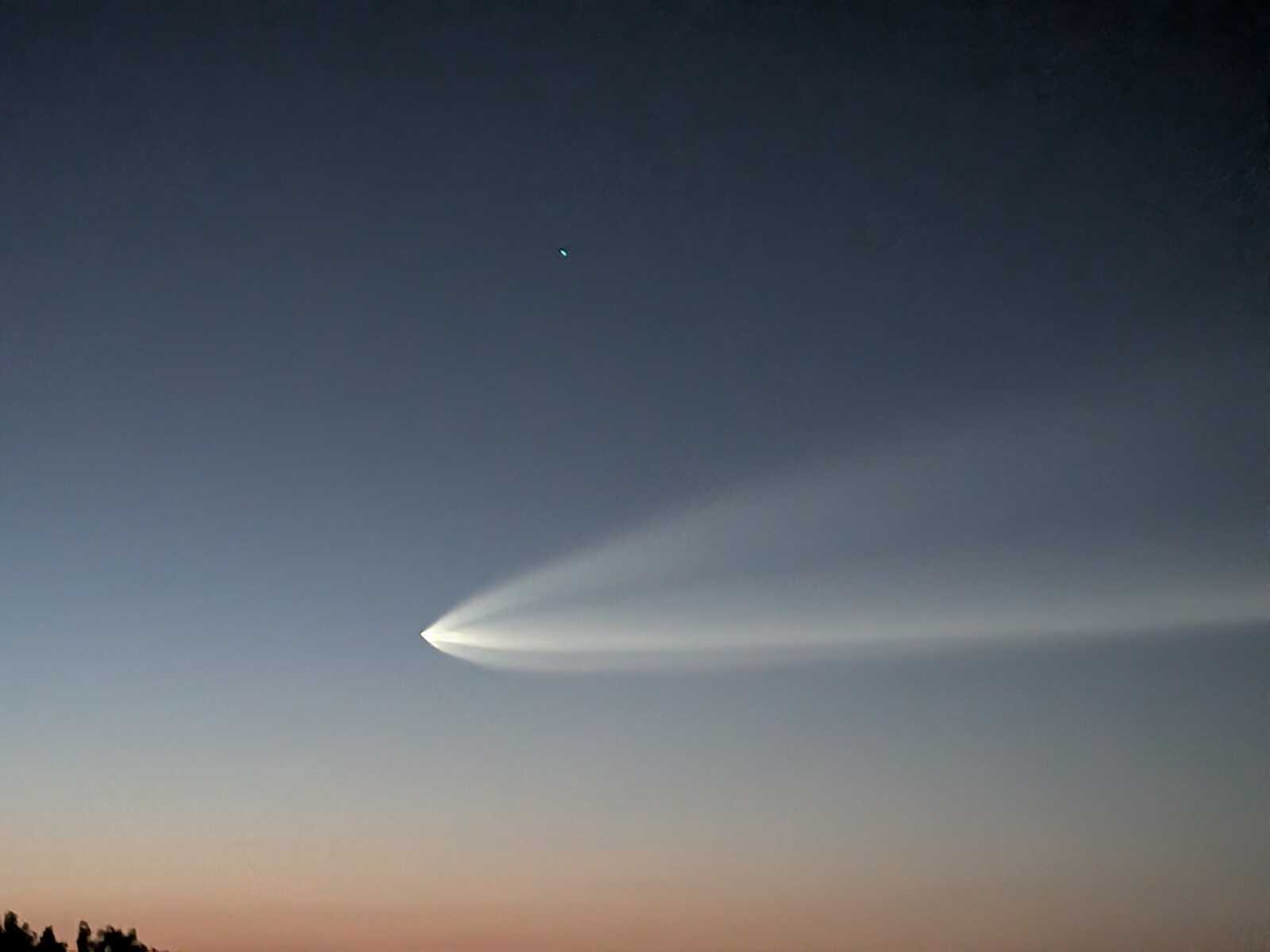 SpaceX's Falcon 9 rocket seen from the Tysons Metro station in the early morning of Aug. 25, 2026 (photo by Chetan B.) | FFXnow Curved jet contrail sweeping across a sunset sky with a small bright dot above it.