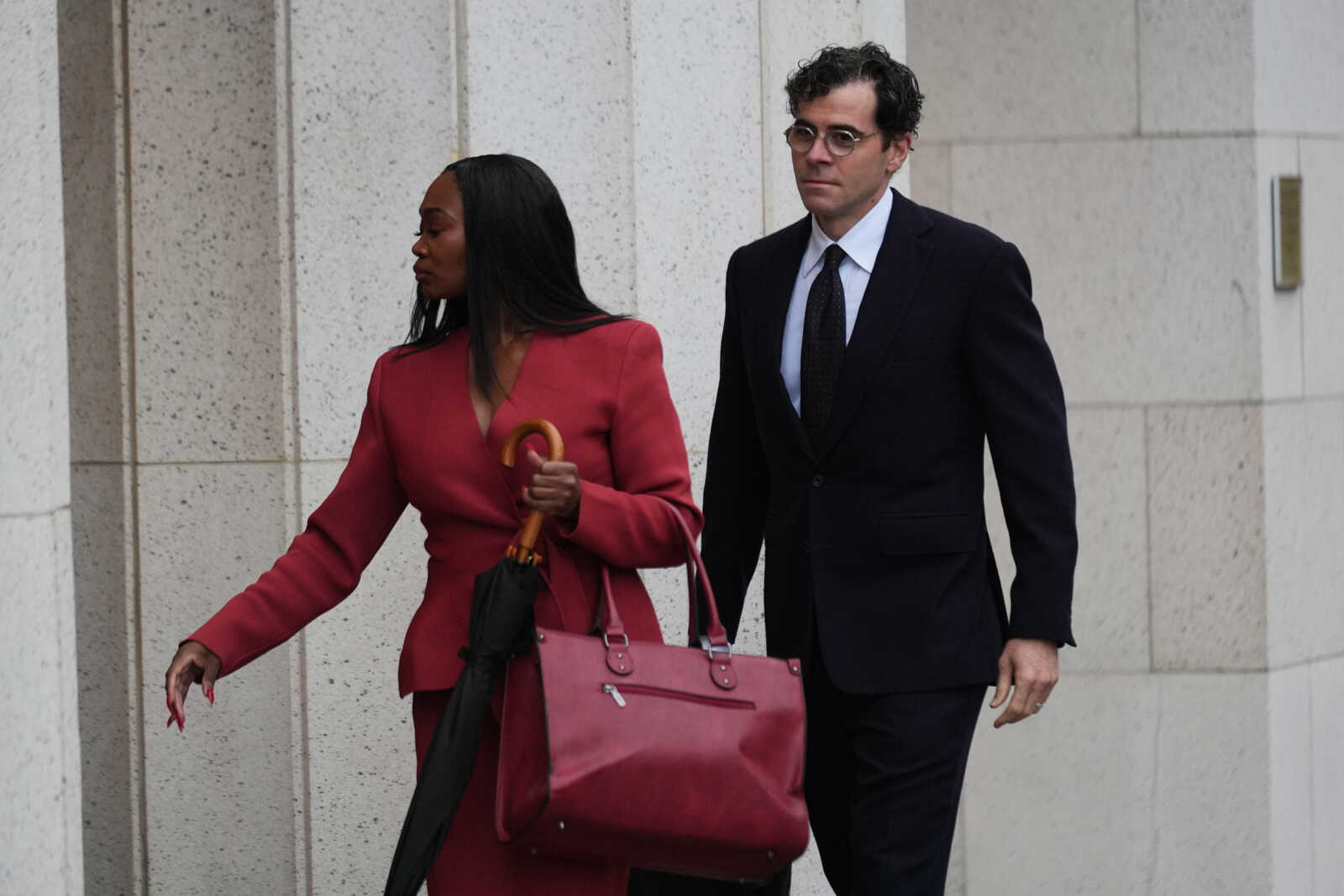 Adam Mosseri, CEO of Instagram, arrives in court to testify in a landmark social media case that seeks to hold tech companies responsible for harms to children, in Los Angeles, Feb. 11, 2026. (AP Photo/Damian Dovarganes, File) | FFXnow Two professionally dressed individuals walk side by side along a stone building; the woman in a red suit carries a pink handbag and a black umbrella, the man in a dark suit watches ahead.