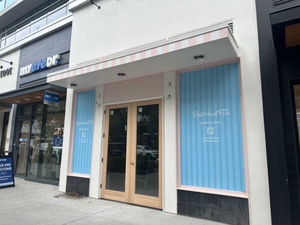 Storefront with a pink-striped awning and glass double doors; blue window panels read 'Bed Head PTs opening soon.'