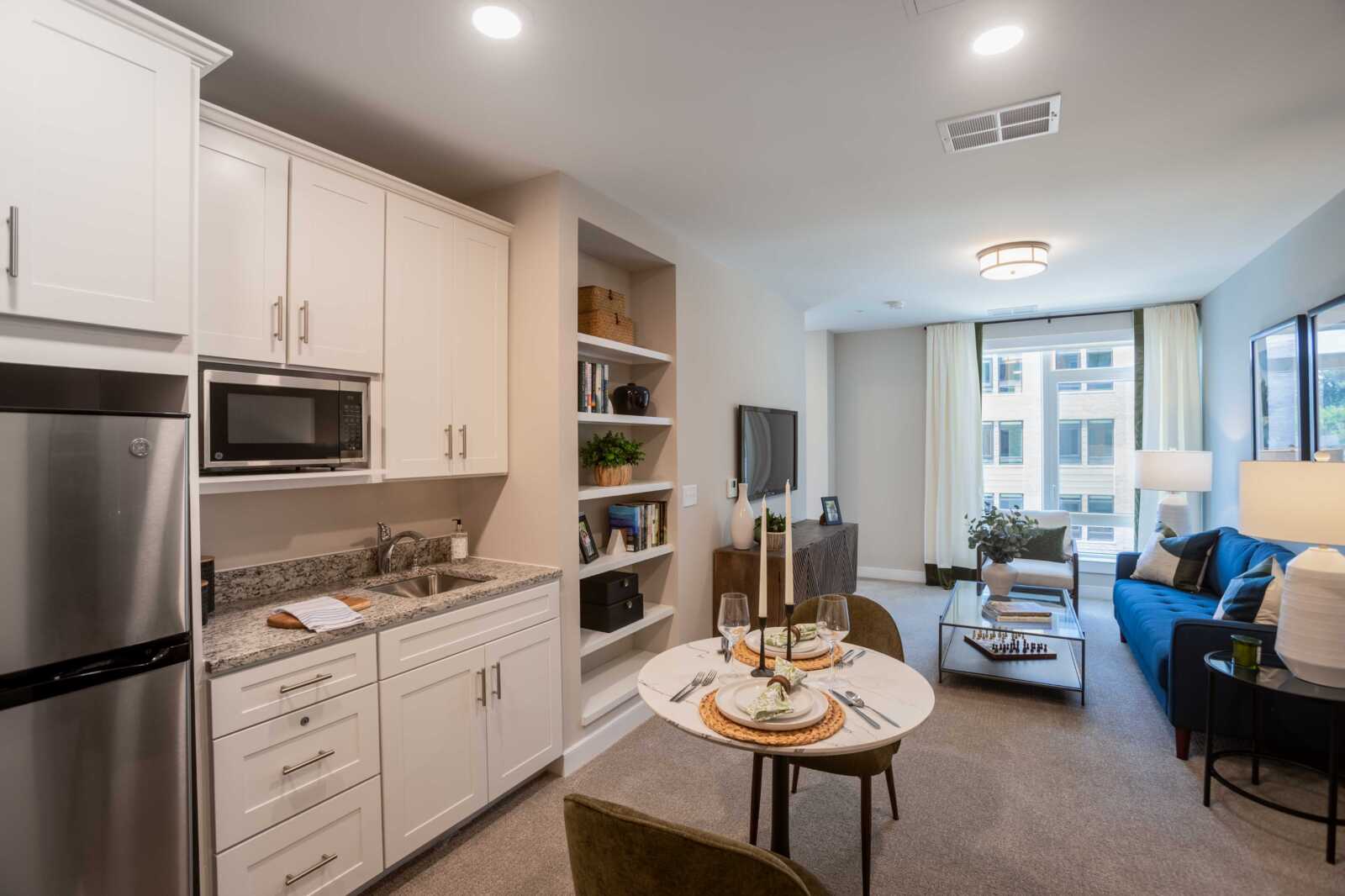 Open-concept living area with white cabinets, stainless fridge, and a small dining table set for two