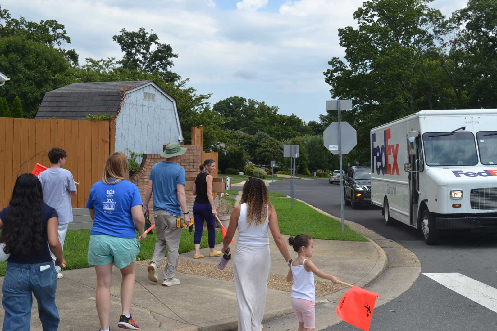 Group of people walking on a sidewalk near a FedEx delivery truck on a residential street.