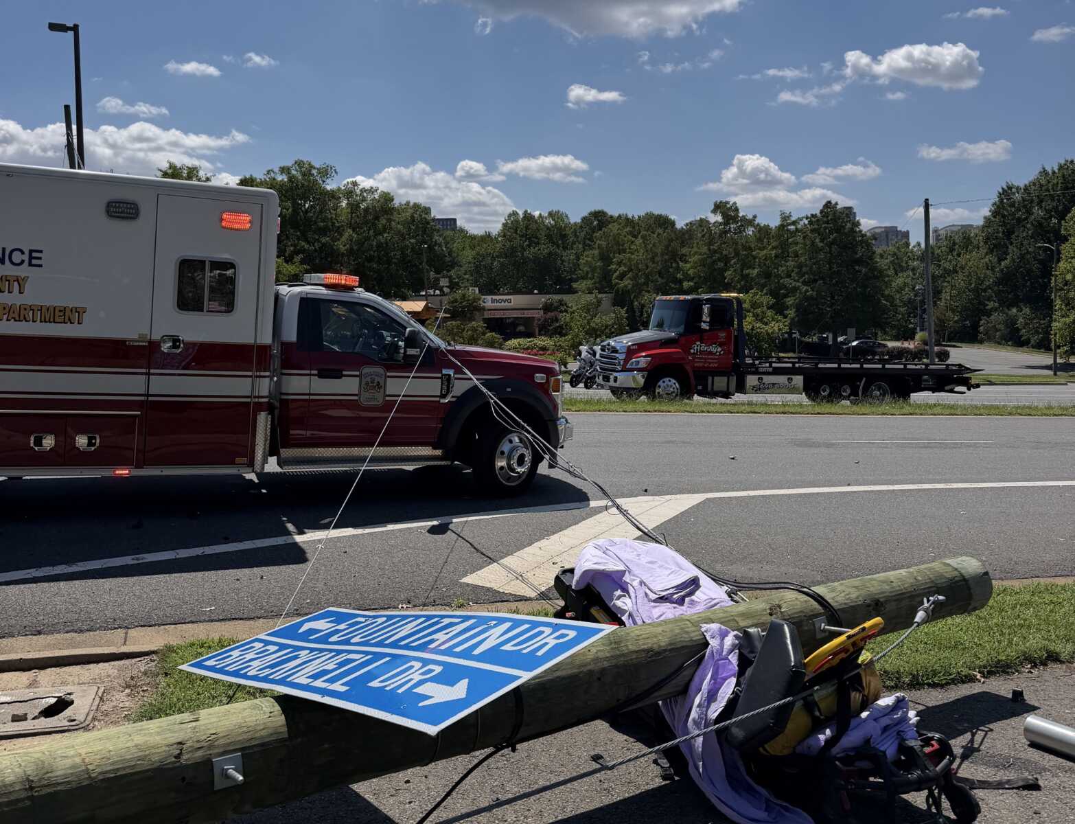 Emergency roadside scene with an ambulance and tow truck, flashing lights active, and a toppled wooden utility pole nearby.
