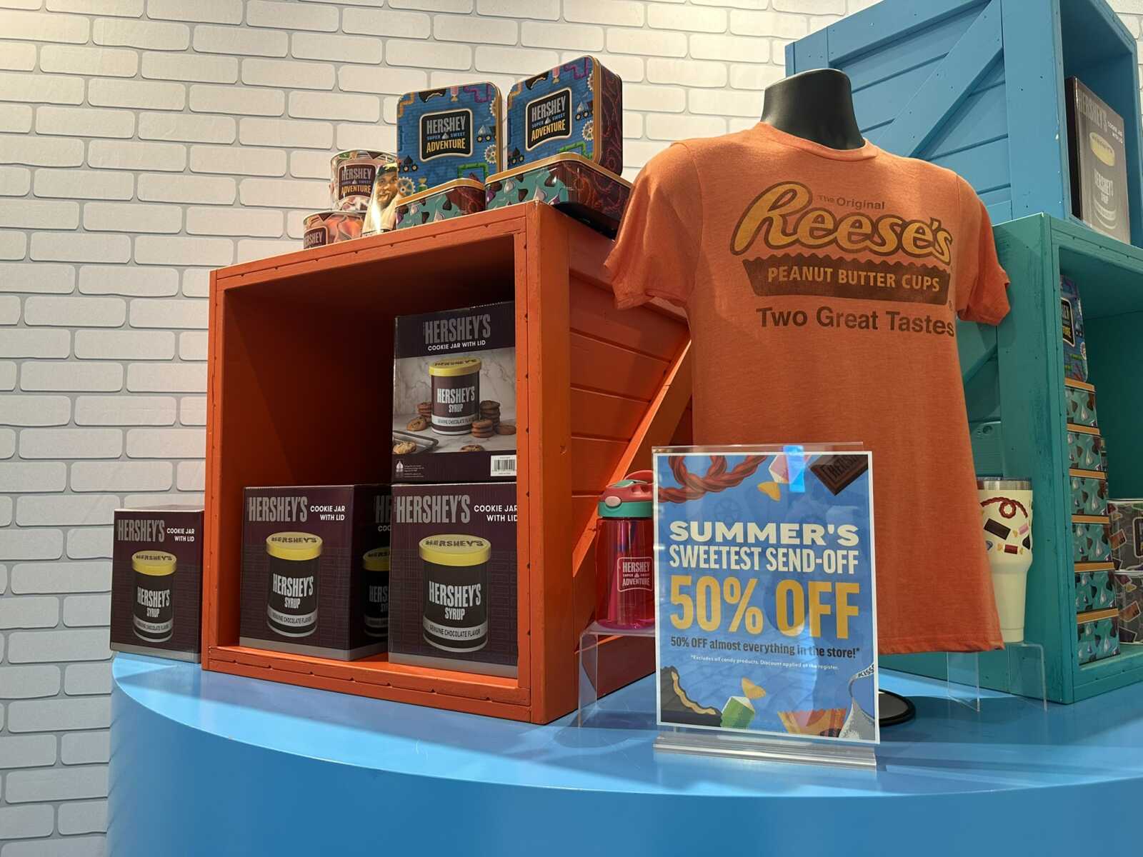 Orange Reese's shirt reads 'Two Great Tastes' beside a Hershey's product display in a bright store setup with a 50% off poster.