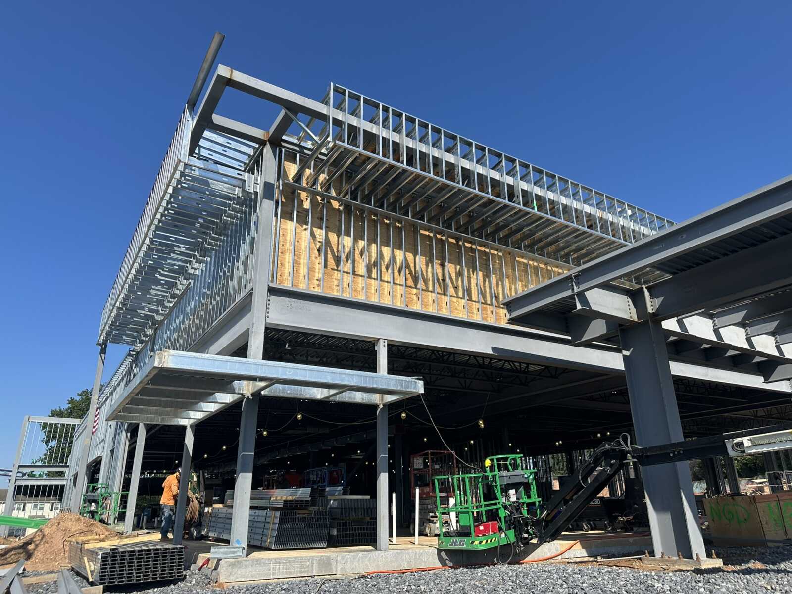 Steel-framed building under construction with exposed metal beams and wooden sheathing against a clear blue sky.