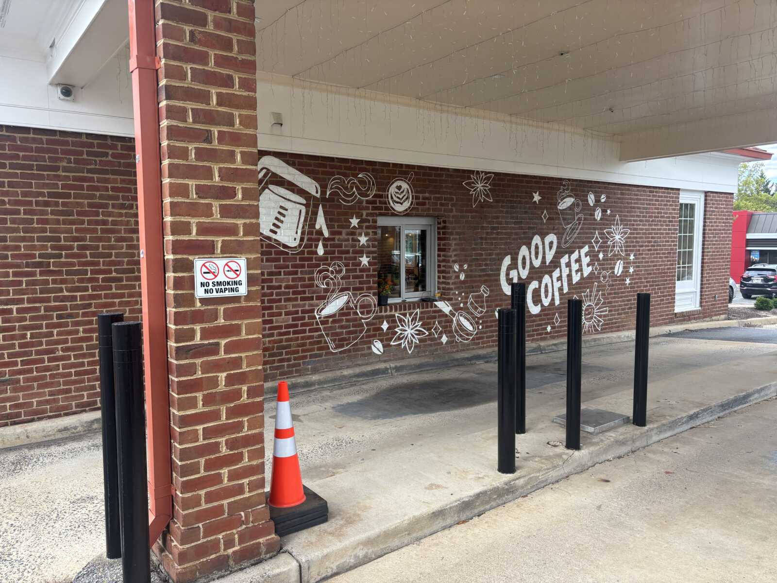 Brick exterior with a white coffee-themed mural that says 'Good Coffee' and coffee-doodle icons beside a window under an overhang.