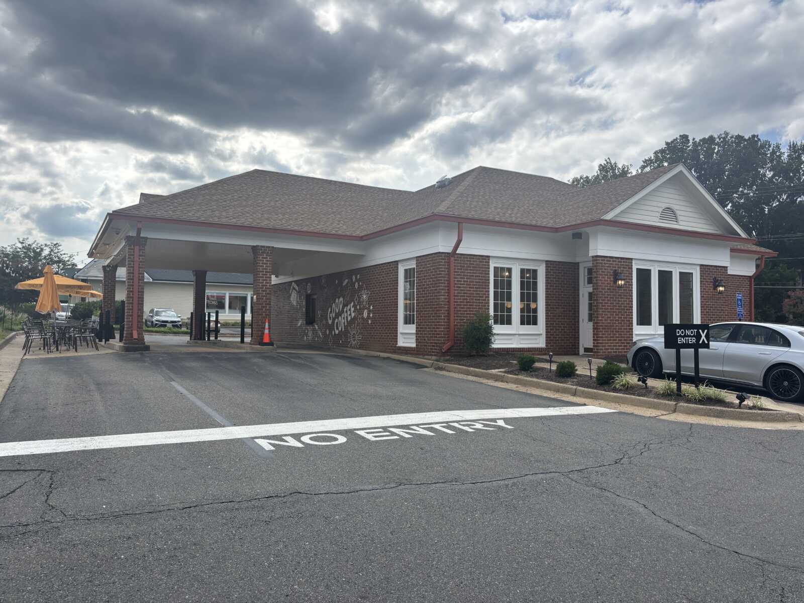 Brick coffee shop with white trim and a covered drive-thru, outdoor seating with orange umbrellas on the left.