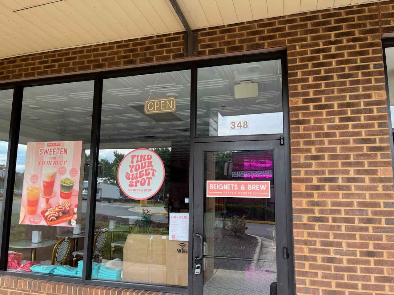 Beignets & Brew storefront with an 'OPEN' sign, large windows showing posters and a menu, brick exterior (address 348).