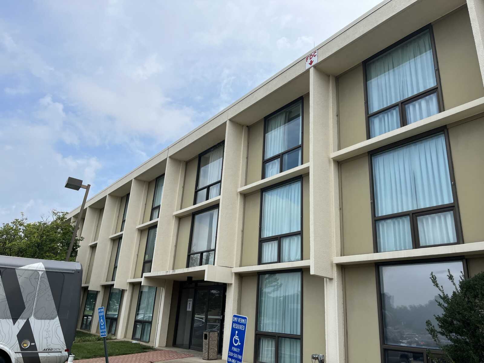 Three-story beige building with tall windows and blue curtains against a blue sky.