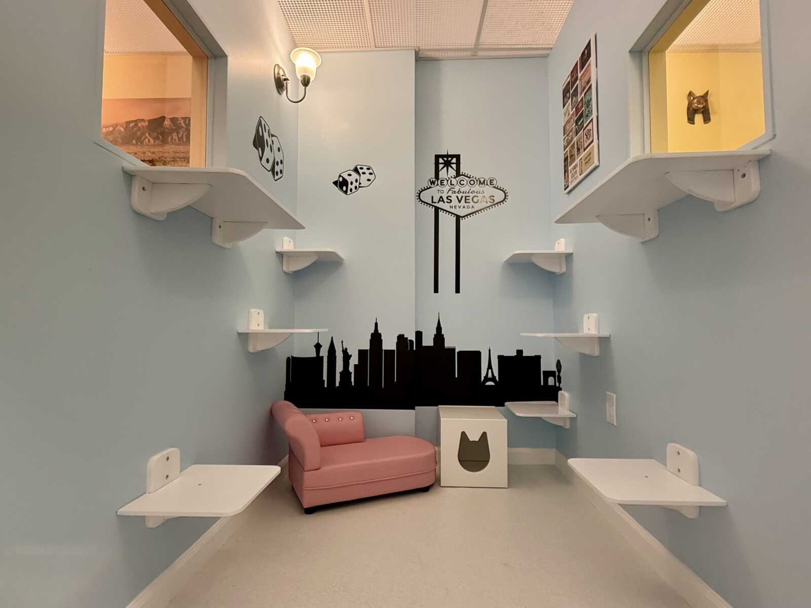 Light blue playroom with white shelves, a pink sofa, and a black Las Vegas skyline mural on the back wall with dice decals above.