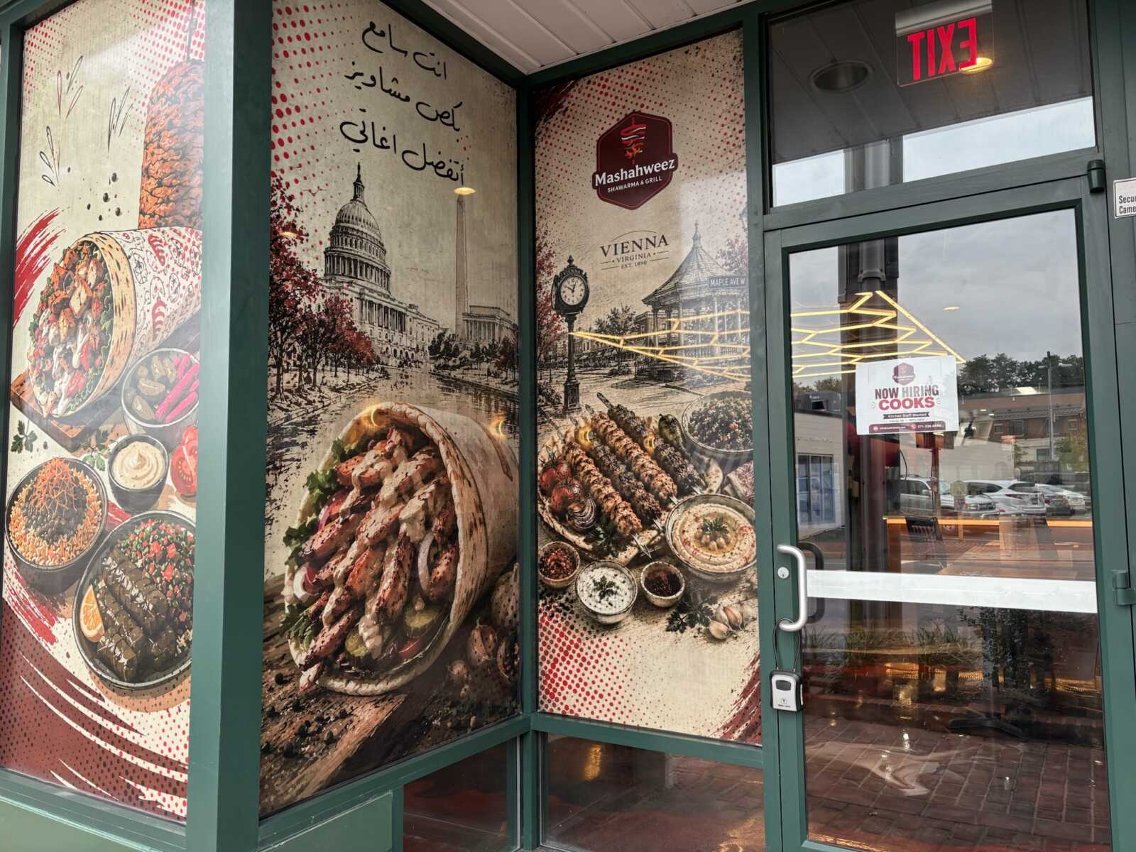 Storefront advertising Mashawheez Shawarma & Grill with images of kebabs, bowls, and a cityscape; door shows a 'Now Hiring Cooks' sign.