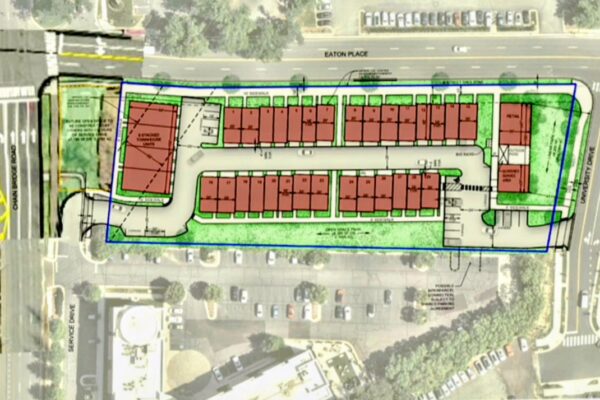 Aerial view of a planned housing development with rows of red-roofed townhouses inside a blue boundary, surrounded by streets and parking lots.