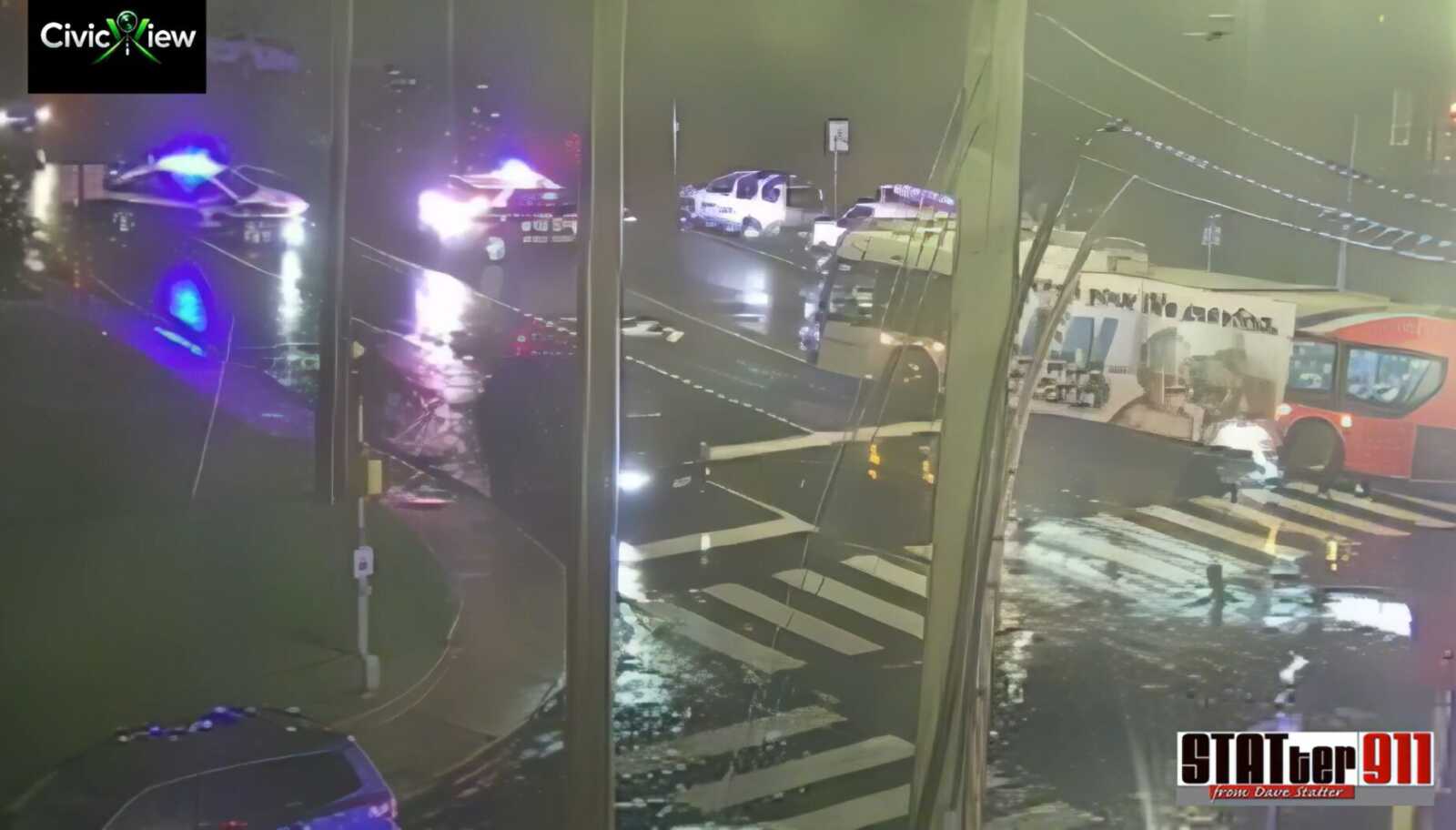 Police respond to a fatal pedestrian crash at Columbia Pike and Carlin Springs Road in Bailey's Crossroads (courtesy Dave Statter/X) | FFXnow Nighttime street scene with police cars flashing blue lights at a rain-soaked intersection, viewed from a glass-fronted building, CivicView logo top-left.