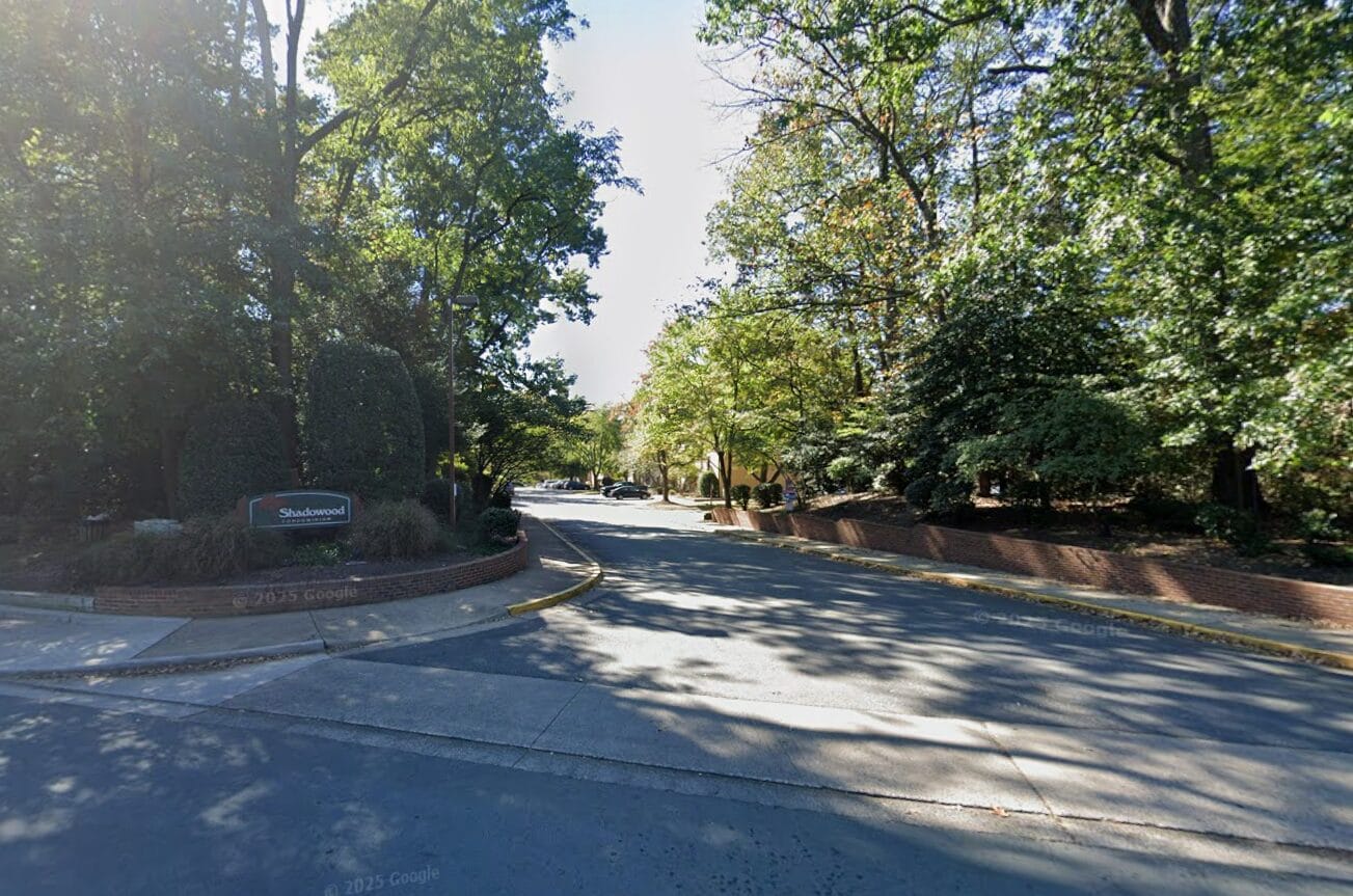 Entrance to the Shadowood Condominiums in Reston (via Google Maps) | FFXnow Entrance to the Shadowood residential community: a brick planter with a sign, and a tree-lined curved road ahead with cars parked in the distance.