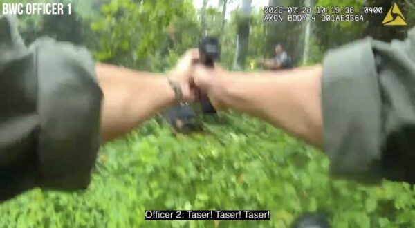 First-person police body‑camera view showing an officer aiming a taser in a leafy outdoor area; on-screen caption says 'Taser! Taser! Taser!'