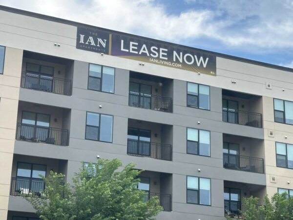 Modern mid-rise apartment building with multiple balconies and a large 'LEASE NOW' banner across the top.