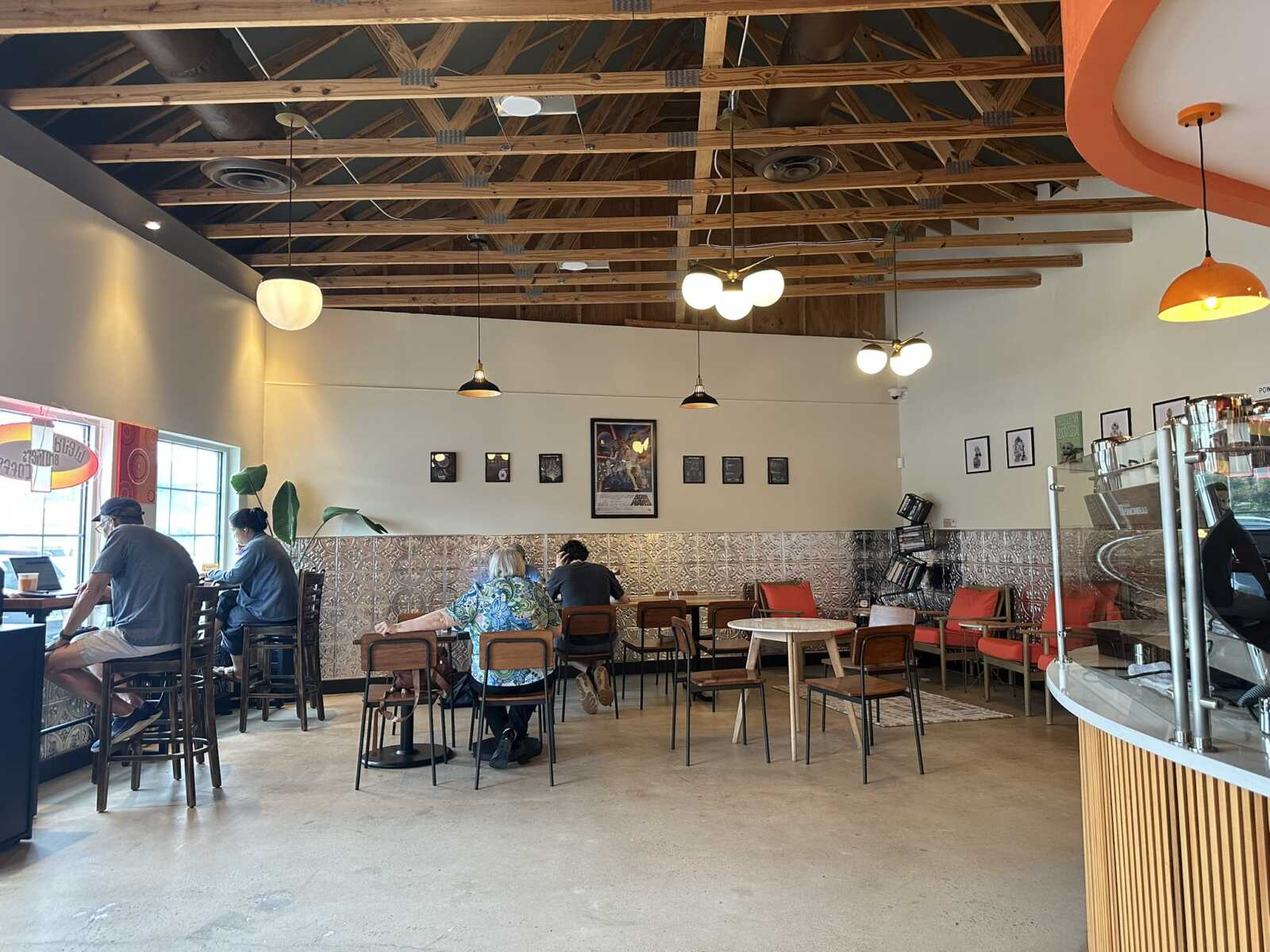 Cafe interior with exposed wooden ceiling, hanging lights, and customers seated at tables near the window.
