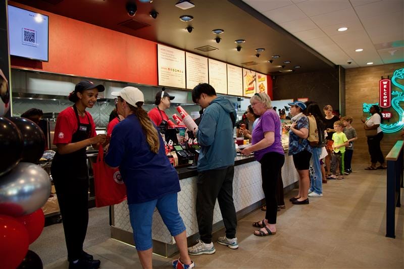 Customers line up at a fast-cood restaurant counter, placing orders with staff in red uniforms.