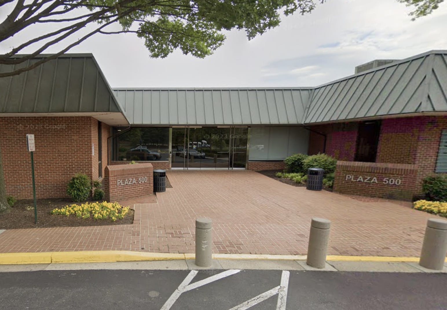 Entrance to a brick plaza building with glass doors labeled Plaza 500, brick walkways, and planters on either side.