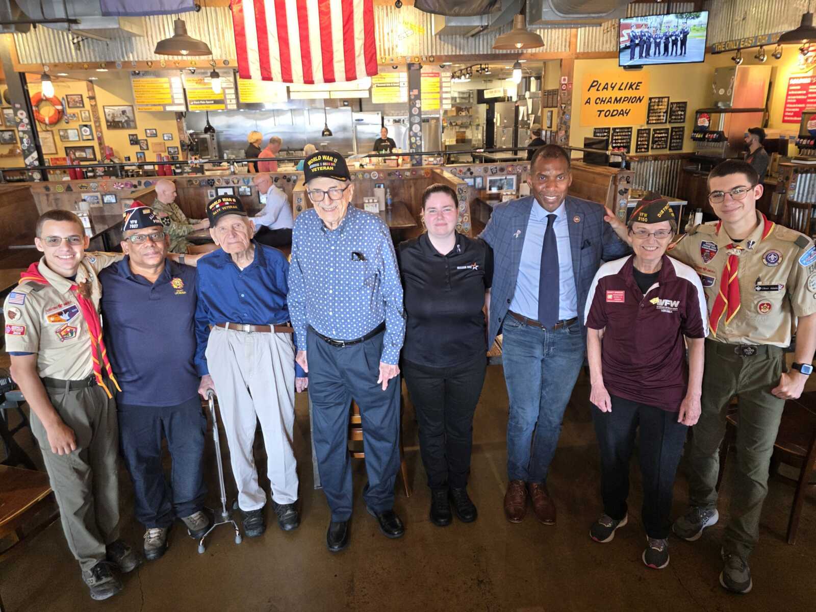 20260902_130612~2 | FFXnow Nine people, including veterans in caps and a staff member in a suit, pose for a group photo inside a restaurant.