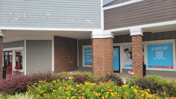 Retail storefront with brick columns and a colorful flower bed in front; signs read 'Retail space for lease' and '2,400 SF'.
