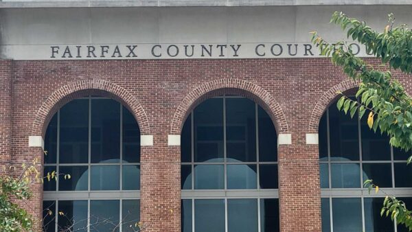 Facade of Fairfax County Courthouse: red brick building with three arched windows and large glass panes, tree branches in foreground