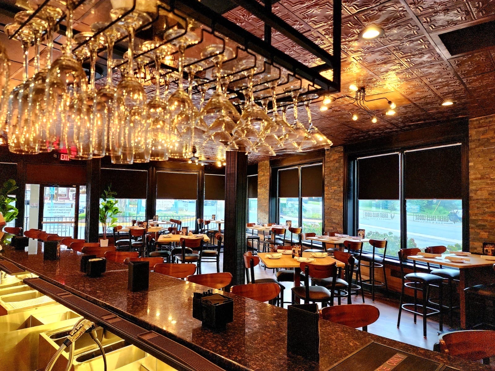 Wine glasses hang upside down from a rack above a glossy black-bar counter in a warm, dimly lit restaurant interior.