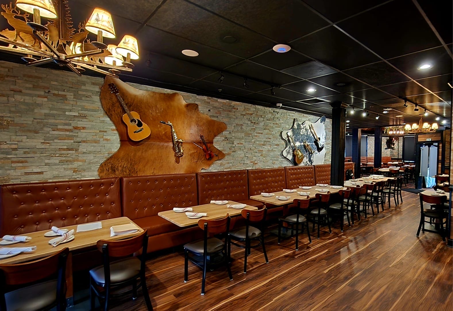 Warm restaurant interior with wooden tables and brown tufted booths, guitars mounted on a stone wall as wall art.