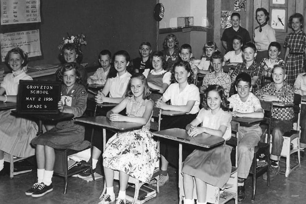 Black-and-white photo of a 1956 Grade 5 class in a classroom, students seated at desks, a sign reads Groveton School, May 2, 1956, Grade 5.