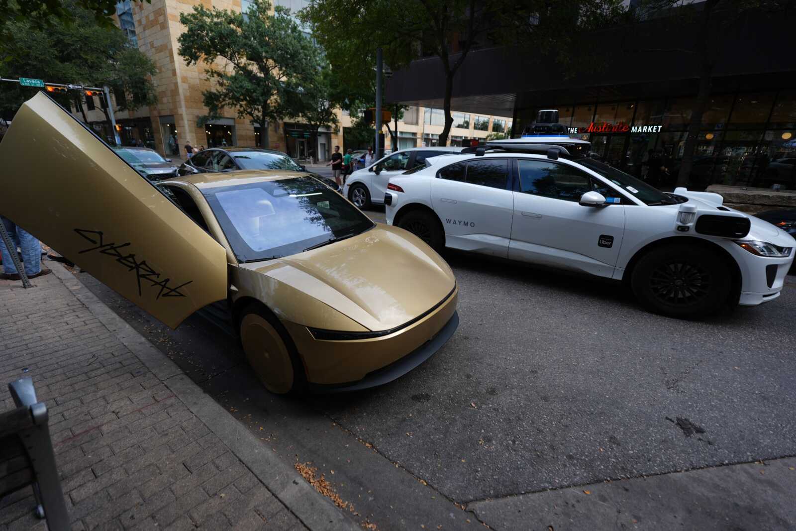 A Tesla Cybercab moves through downtown Austin, Texas, Thursday, Sept. 3, 2026. (AP Photo/Eric Gay) | FFXnow Gold Fisker Karma with its gull-wing doors open, parked on a city street beside a white Waymo Uber autonomous car.