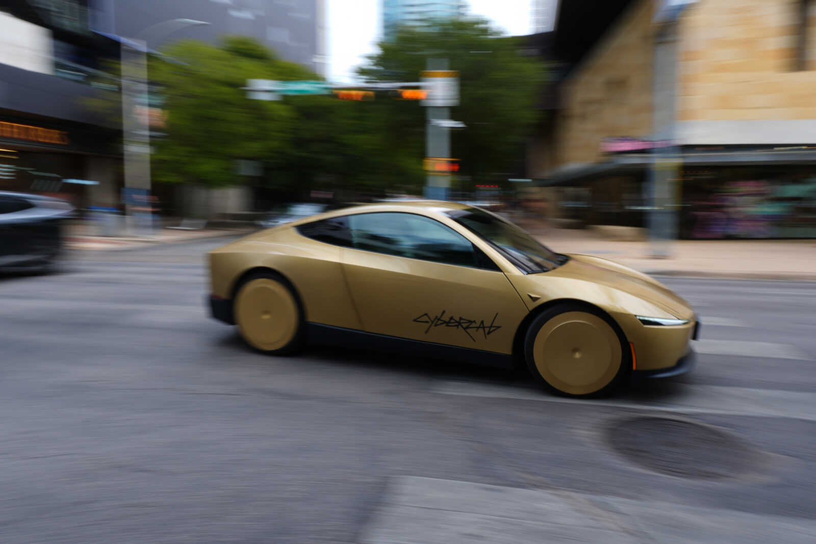 Golden futuristic sports car speeding down a city street, motion blur surrounding it along storefronts and traffic lights.