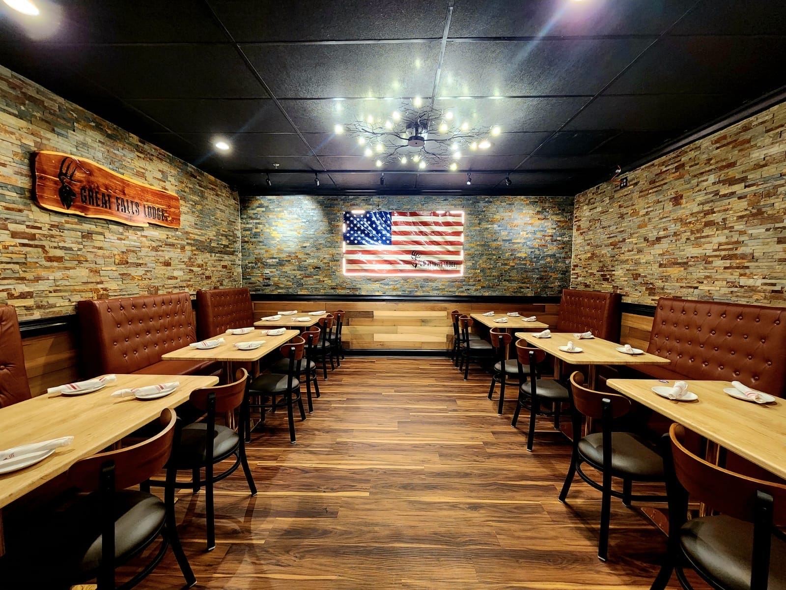 Dining area with stone walls, wooden floors, and red leather booths; American flag mural lit on the back wall.