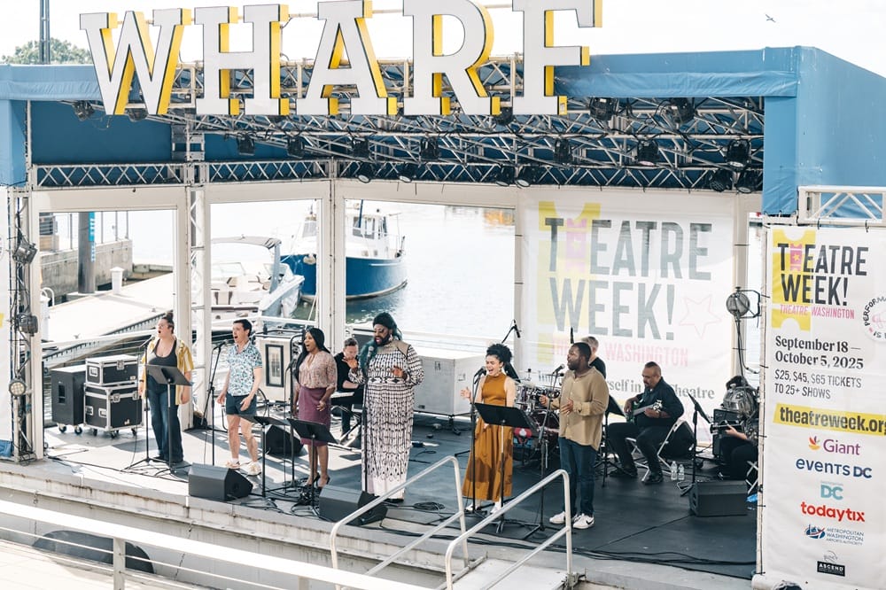 Free concert at The Wharf in D.C. for Theatre Week 2025 (courtesy Theatre Washington) | FFXnow A diverse group of singers performing on an outdoor waterfront stage under a blue canopy, with Theatre Week banners nearby.