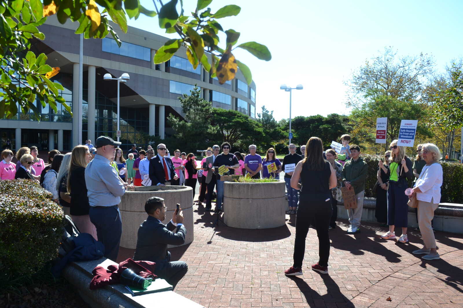 Group of people protesting outside a modern office building, some holding signs and chatting in daylight.